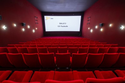 Salle de cinéma avec des sièges rouges, un écran géant affichant ’Salle 14, 241 fauteuils’ et un éclairage tamisé.