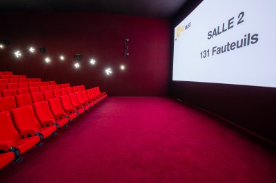 Salle de cinéma avec des sièges rouges, un écran géant affichant ’Salle 14, 241 fauteuils’ et un éclairage tamisé.
