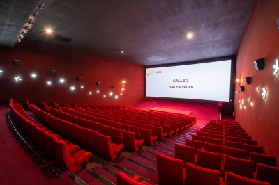 Salle de cinéma avec des sièges rouges, un écran géant affichant ’Salle 14, 241 fauteuils’ et un éclairage tamisé.