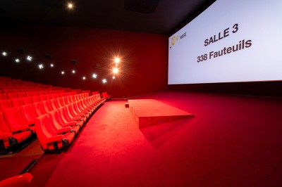 Salle de cinéma avec des sièges rouges, un écran géant affichant ’Salle 14, 241 fauteuils’ et un éclairage tamisé.