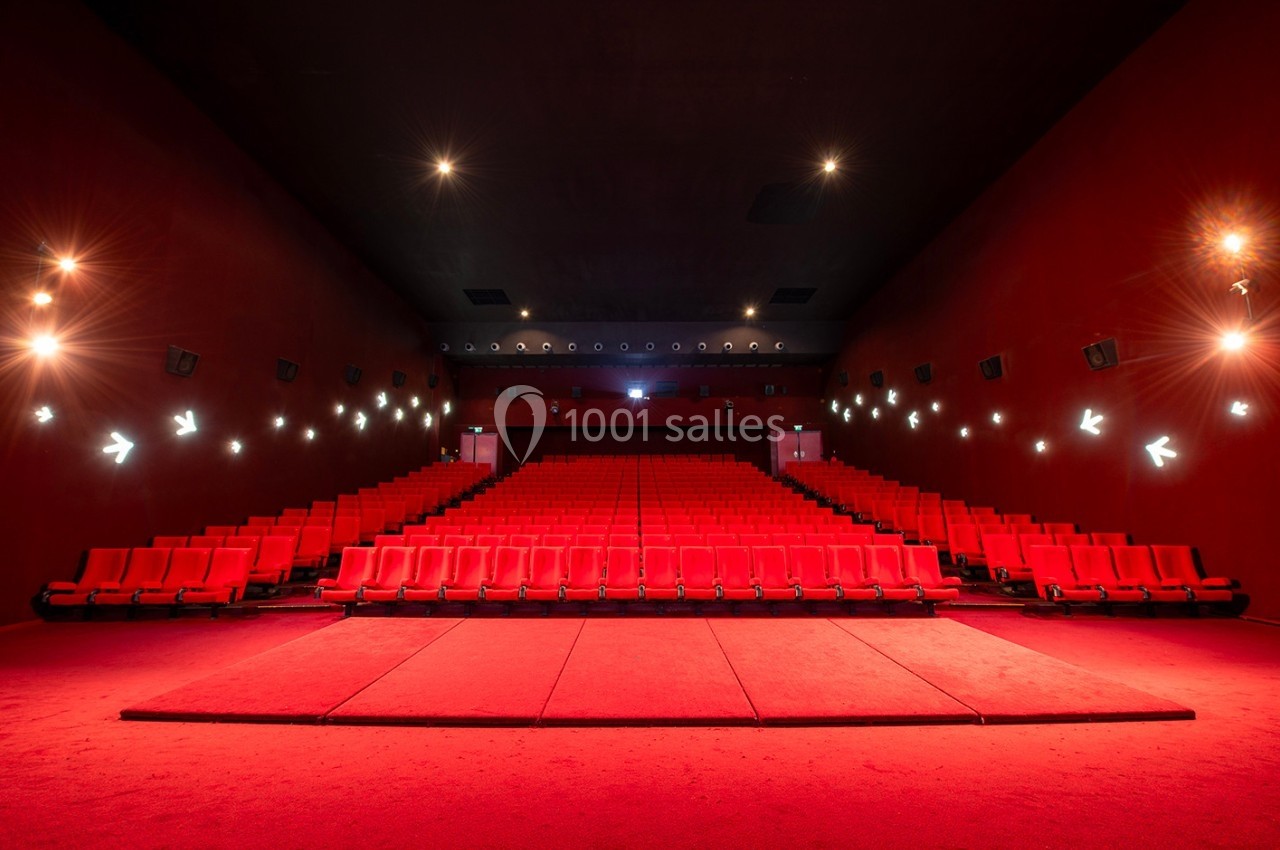 Salle de cinéma vide avec des rangées de sièges rouges et un éclairage tamisé sur les murs.