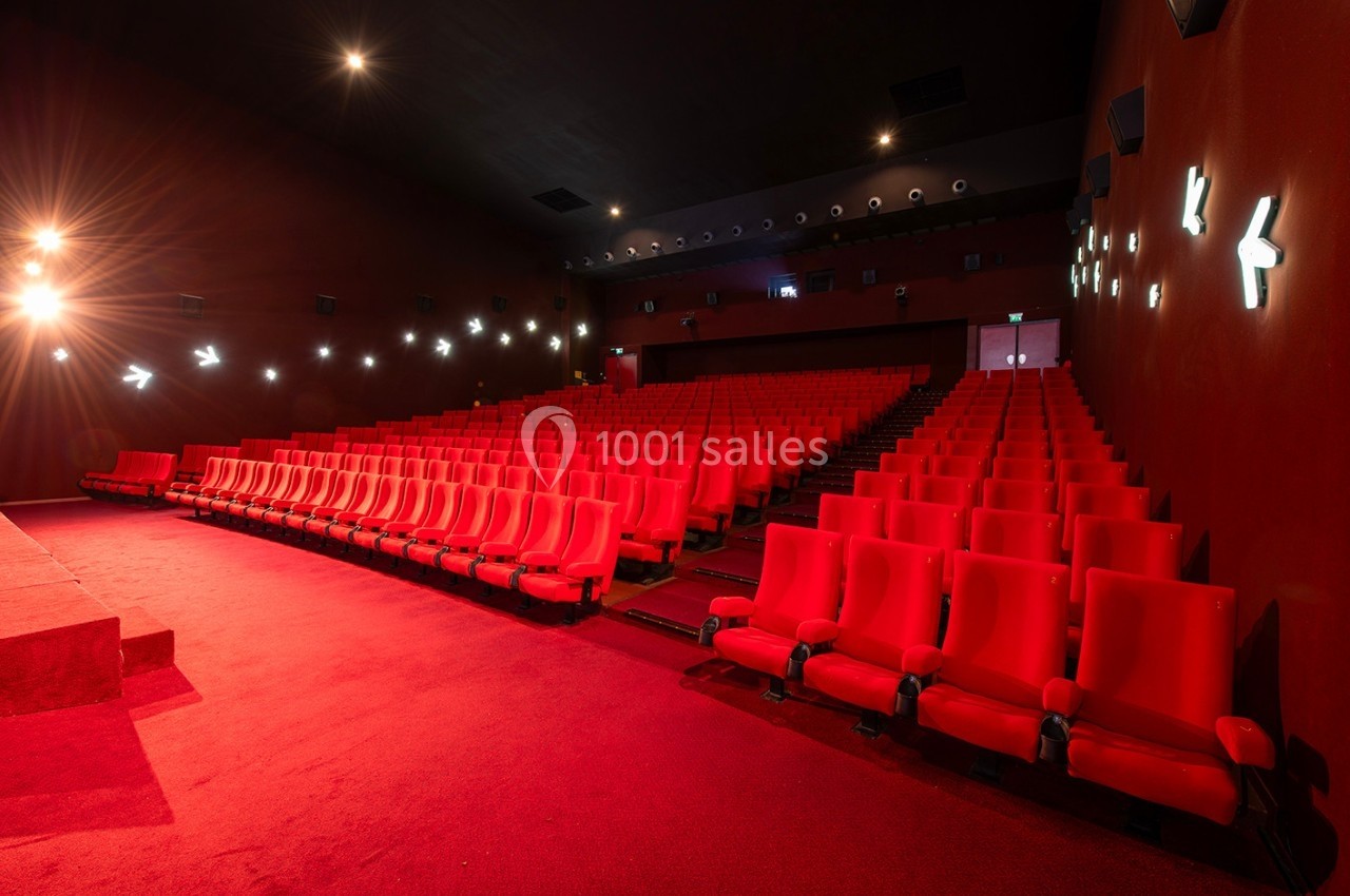 Salle de cinéma vide avec des rangées de fauteuils rouges et un éclairage tamisé.