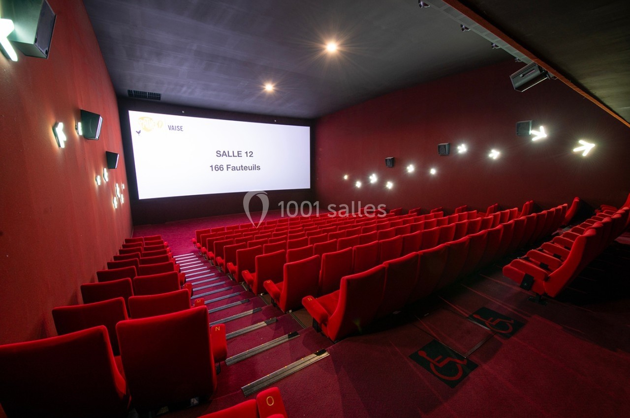 Salle de cinéma vide avec des rangées de fauteuils rouges, écran blanc et éclairage tamisé.