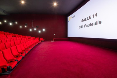 Salle de cinéma avec des sièges rouges, un écran géant affichant ’Salle 14, 241 fauteuils’ et un éclairage tamisé.
