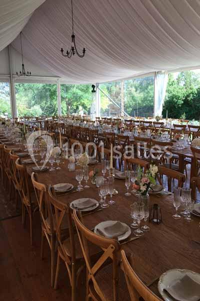 Grande salle de réception sous chapiteau avec longues tables en bois, vaisselle élégante et décor floral.