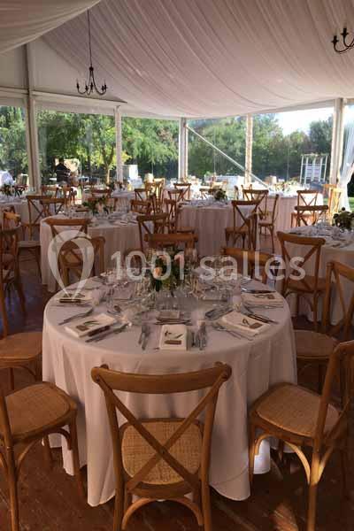 Salle de réception décorée avec des tables rondes, nappes blanches, chaises en bois et arrangements floraux.