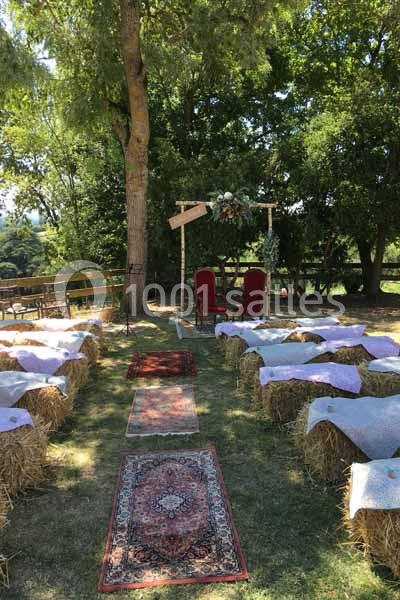 Allée centrale bordée de bottes de paille recouvertes de tissus, menant à une arche décorée pour une cérémonie en plein air.
