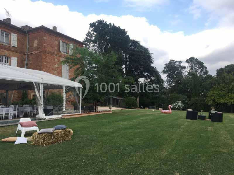 Pelouse avec des bottes de foin, coussins, une tente blanche et un bâtiment en briques rouges en arrière-plan.