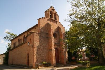 Église en briques rouges avec clocher-mur, entourée d'arbres et située dans un environnement rural.
