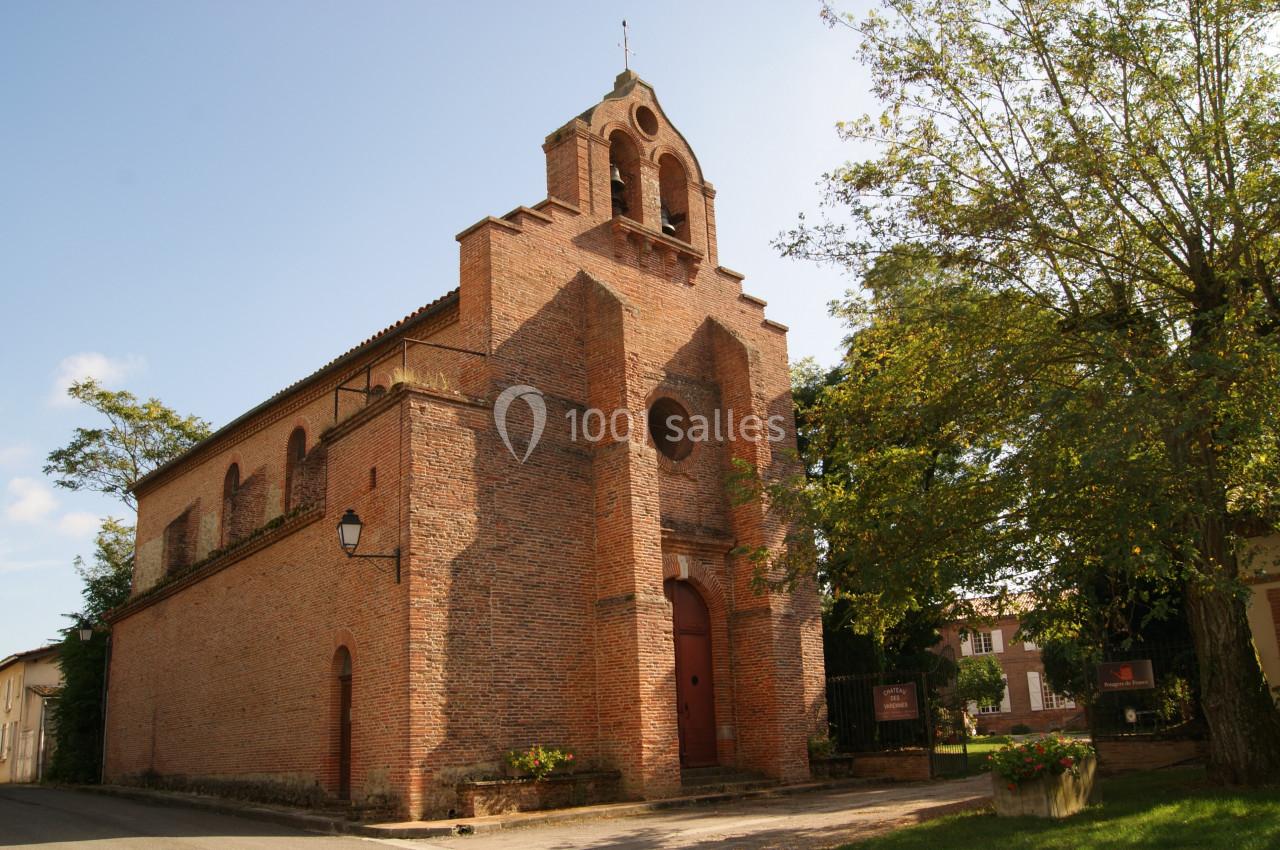 Église en briques rouges avec clocher-mur, entourée d'arbres et située dans un environnement rural.