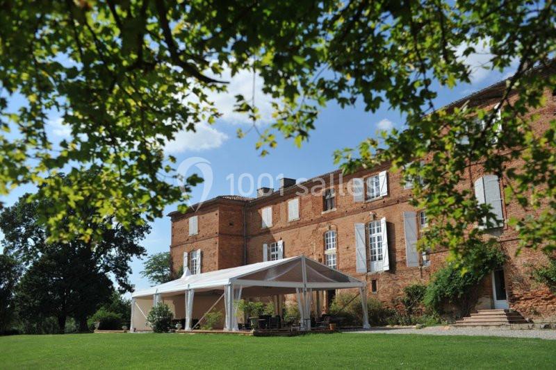Bâtisse en briques rouges avec des volets blancs, une tente blanche installée sur une pelouse verte, arbres au premier plan.