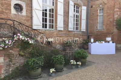 Statue en pierre près d'un escalier en briques, avec des hortensias roses en pots au premier plan.