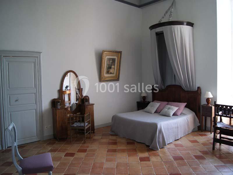 Chambre lumineuse avec lit à baldaquin, commode avec miroir, chaises en bois et sol en carreaux de terre cuite.