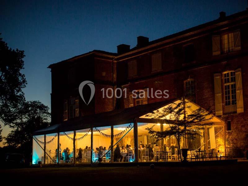 Tente éclairée installée devant un bâtiment en briques, accueillant des invités en soirée.