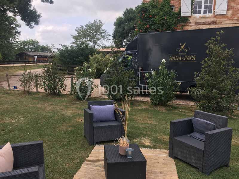 Mobilier de jardin avec fauteuils et table basse sur une pelouse, près d'un camion noir stationné devant un bâtiment en…