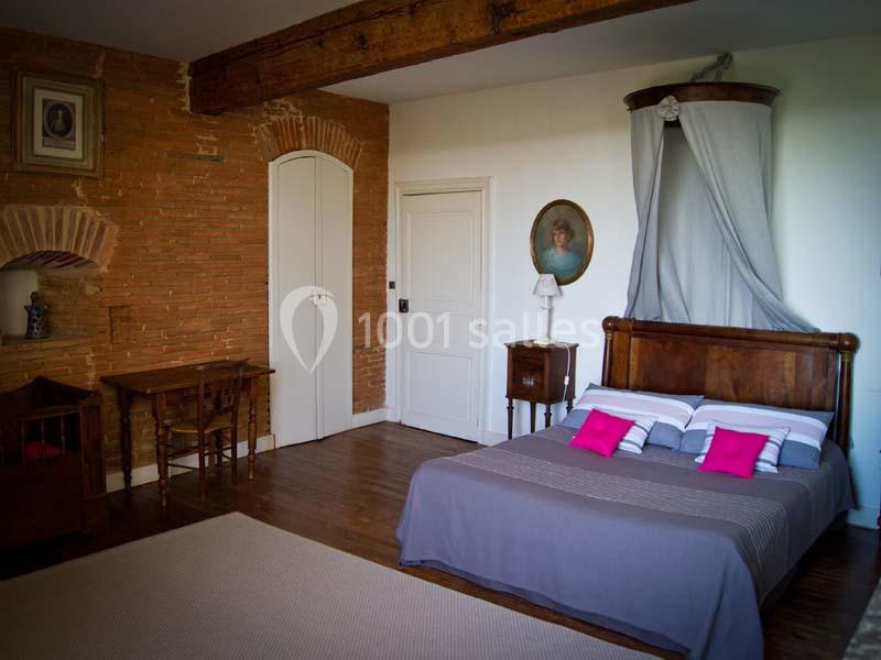 Chambre avec lit double en bois, murs en briques et plâtre, poutre apparente, bureau et décoration classique.