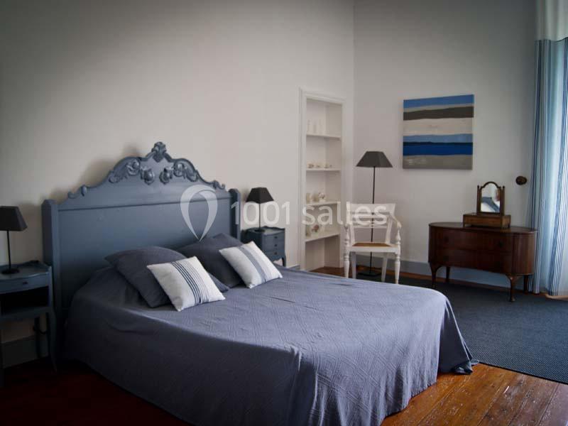 Chambre lumineuse avec un lit double, tête de lit bleue, tables de chevet, commode et décoration minimaliste.