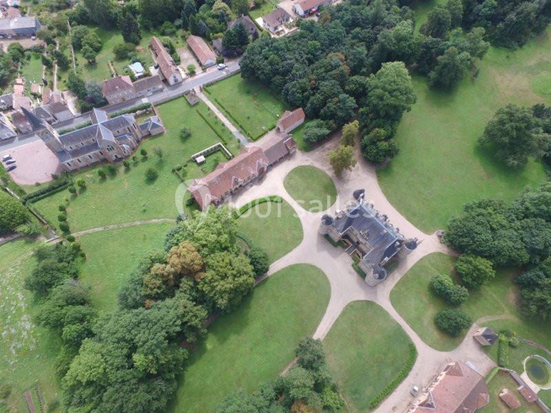 Vue aérienne d'un domaine avec un château entouré de jardins, d'arbres et de bâtiments annexes dans un cadre rural.