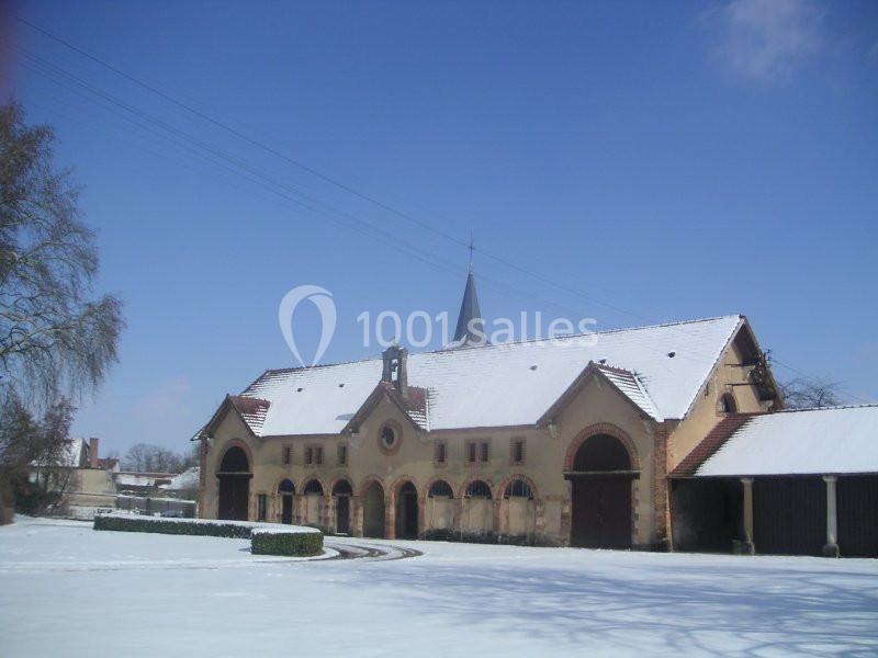 Bâtiment en pierre avec toit enneigé, clocher central et ciel dégagé en arrière-plan.