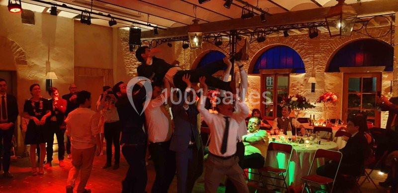 Des invités soulèvent une personne en costume lors d'une fête dans une salle éclairée et décorée.