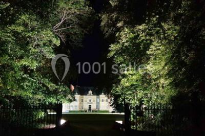 Miniature Location salle Beaulon (Allier) - Château de Beaulon #27 Vue nocturne d'un château illuminé entouré d'arbres, avec une allée sombre au premier plan.