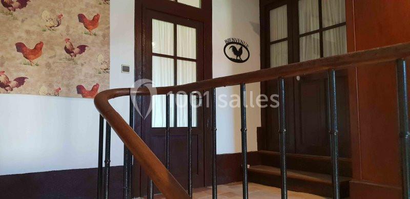 Entrée d'une maison avec une rampe en bois, une porte vitrée et une décoration murale avec des motifs de poules.