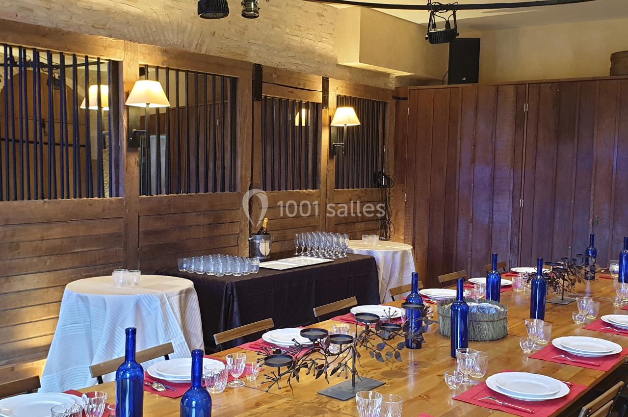 Salle à manger avec une grande table dressée, des bouteilles bleues et des murs en bois éclairés par des appliques.