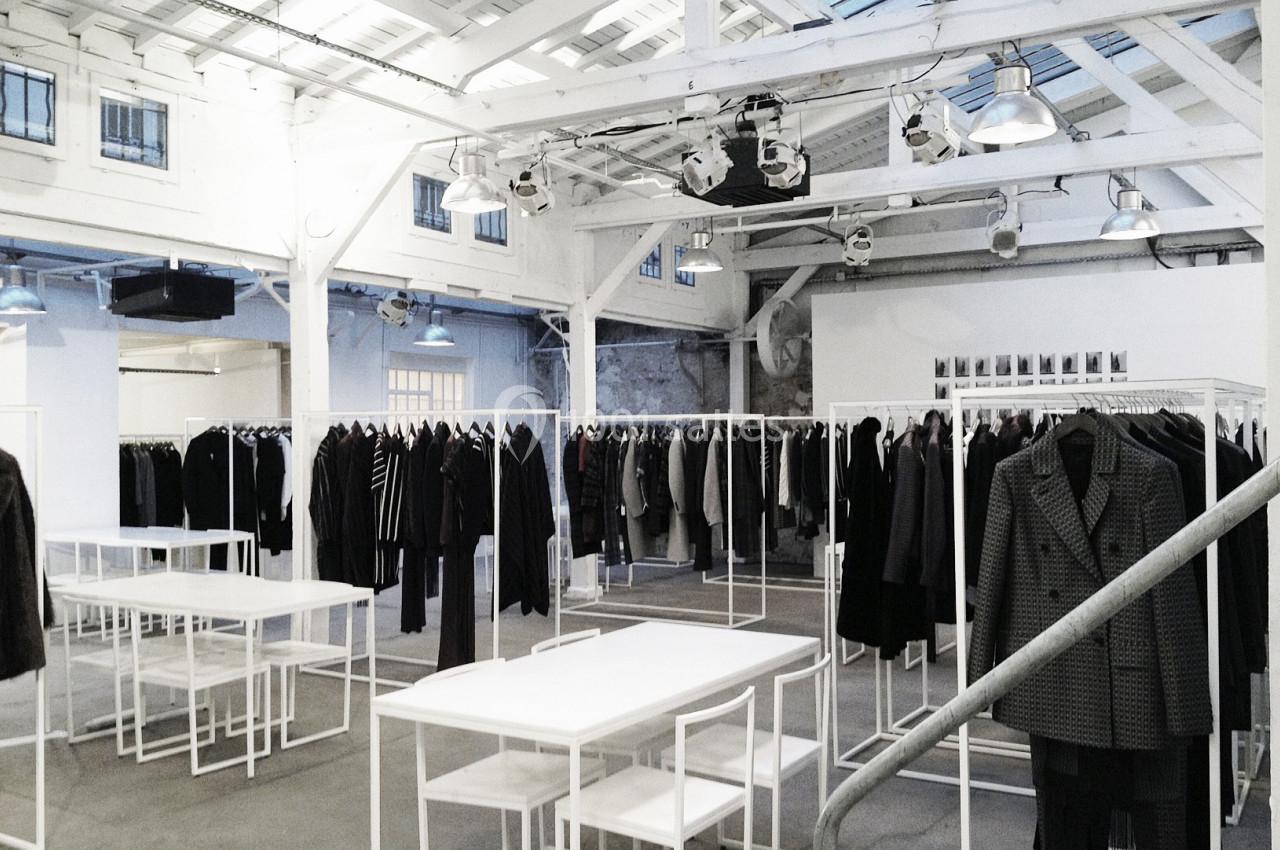 Salle lumineuse avec des portants de vêtements élégants, des tables blanches et une structure en bois peint en blanc.