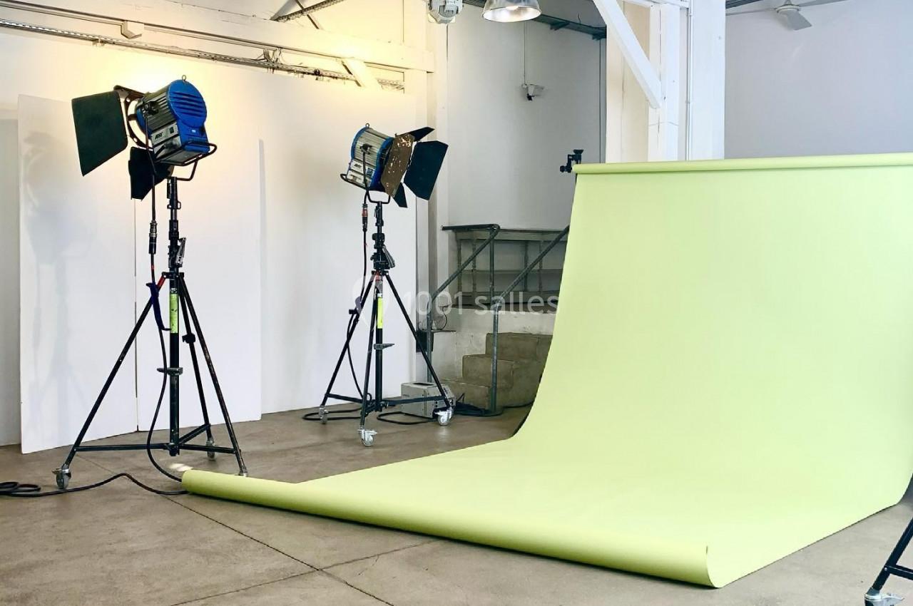 Studio photo avec fond vert clair déroulé, éclairages sur trépieds et murs blancs en arrière-plan.