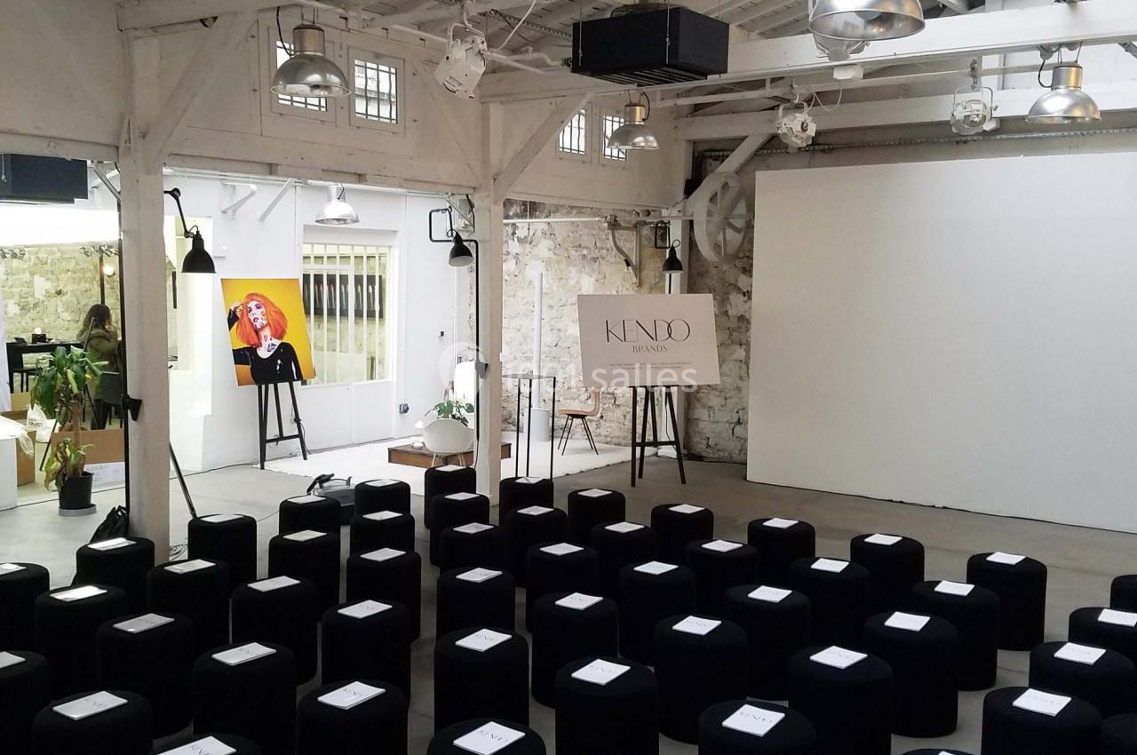 Salle lumineuse avec des sièges noirs alignés, un écran blanc et un chevalet portant une affiche ’Kendo’.