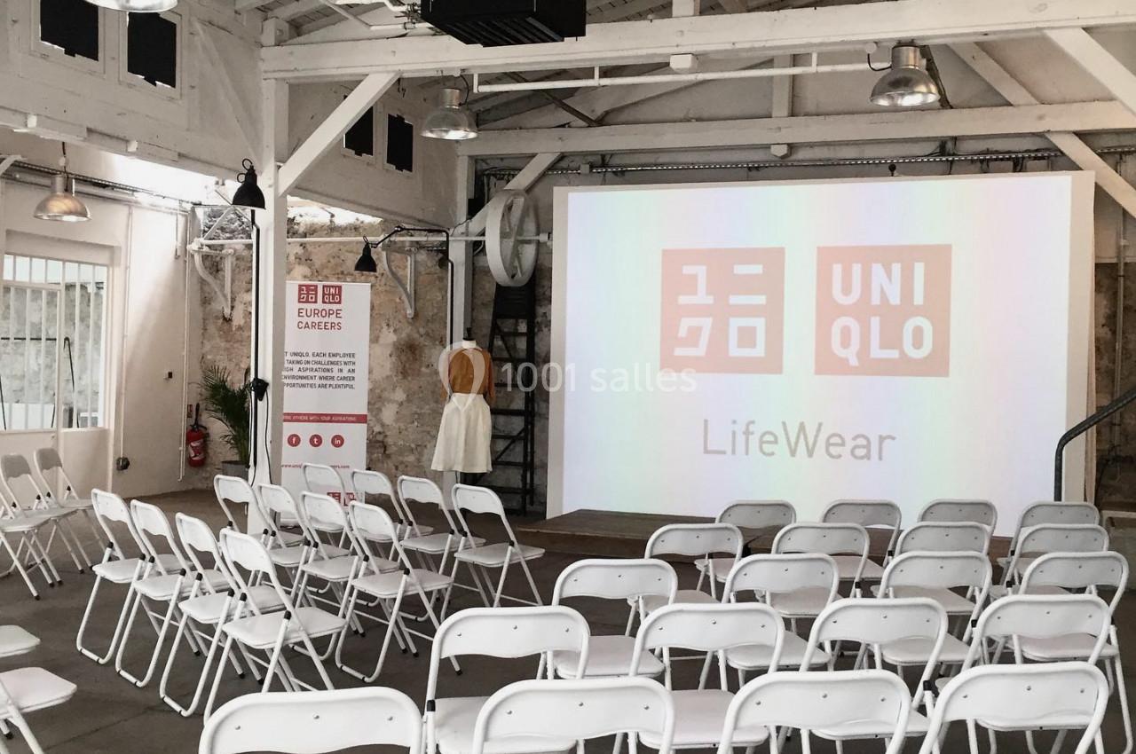 Salle lumineuse avec des chaises blanches alignées face à un écran de projection affichant le logo Uniqlo.