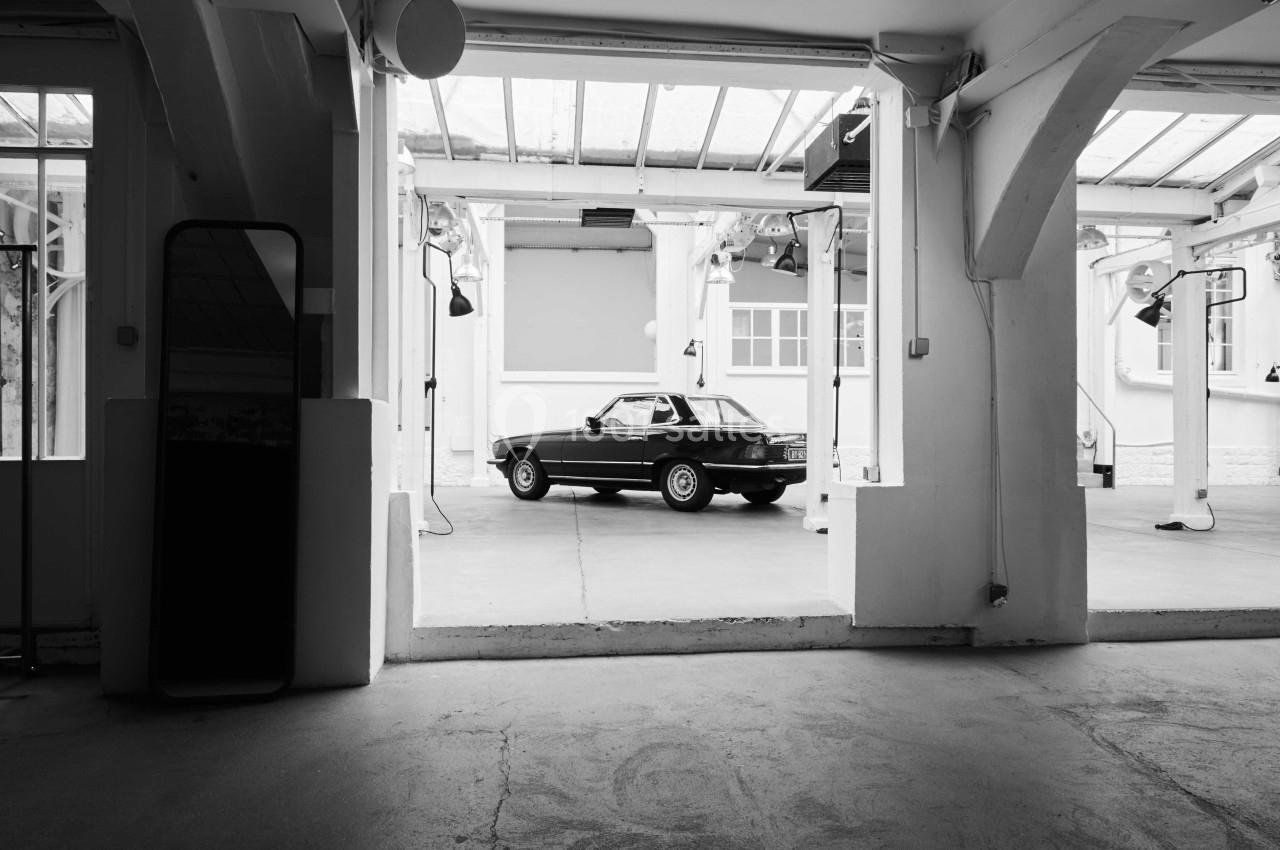 Voiture ancienne noire garée dans un espace intérieur lumineux avec des structures en béton et des verrières.