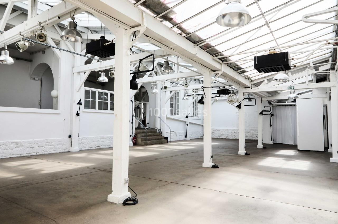 Espace intérieur lumineux avec structure métallique blanche, sol en béton et toit en verrière.