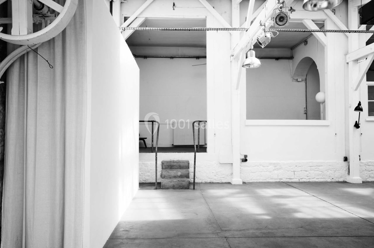 Intérieur d'un espace lumineux avec murs blancs, sol en béton, escalier central et structures métalliques apparentes.