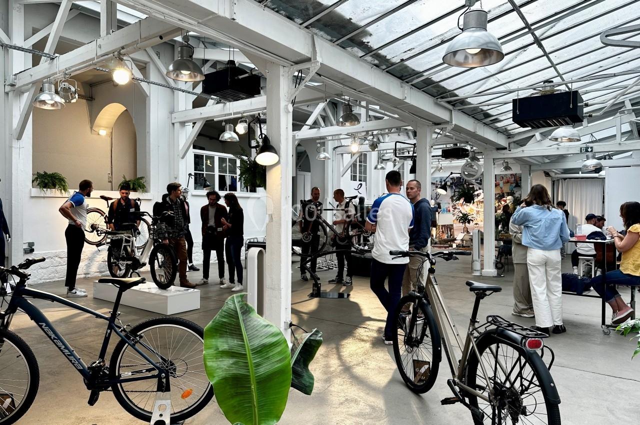 Des personnes discutent et observent des vélos exposés dans un espace lumineux avec une structure en verrière.