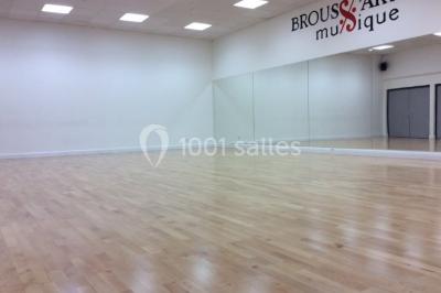 Vue d'un jardin clôturé avec pelouse, deux pots rouges contenant des plantes et un premier plan de feuilles vertes.