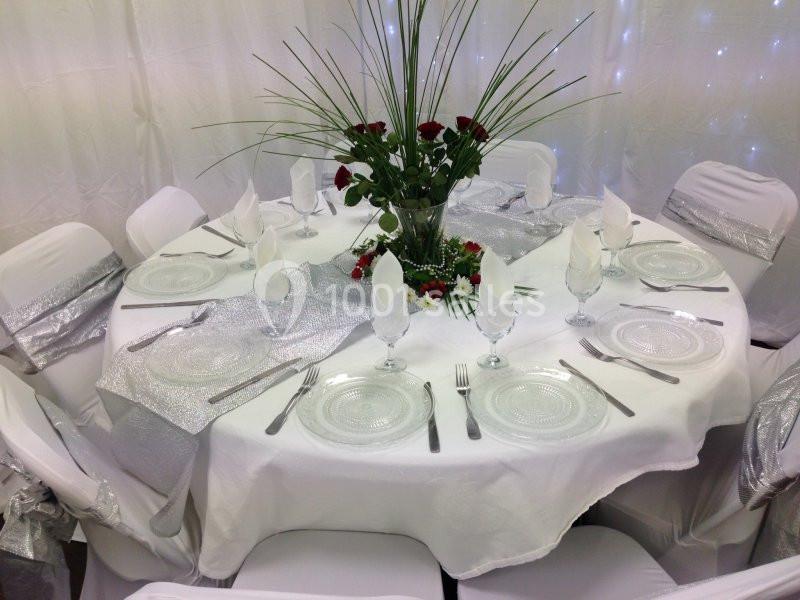 Table ronde élégamment dressée avec nappes blanches, serviettes pliées, vaisselle transparente et décoration florale…