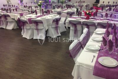 Vue d'un jardin clôturé avec pelouse, deux pots rouges contenant des plantes et un premier plan de feuilles vertes.