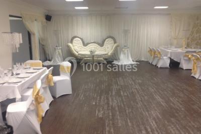 Vue d'un jardin clôturé avec pelouse, deux pots rouges contenant des plantes et un premier plan de feuilles vertes.