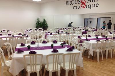 Vue d'un jardin clôturé avec pelouse, deux pots rouges contenant des plantes et un premier plan de feuilles vertes.