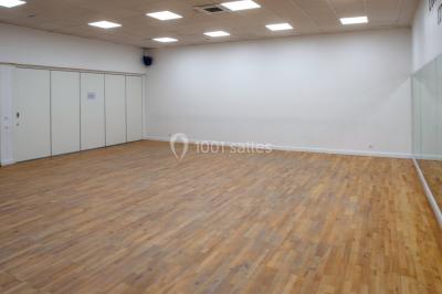 Vue d'un jardin clôturé avec pelouse, deux pots rouges contenant des plantes et un premier plan de feuilles vertes.