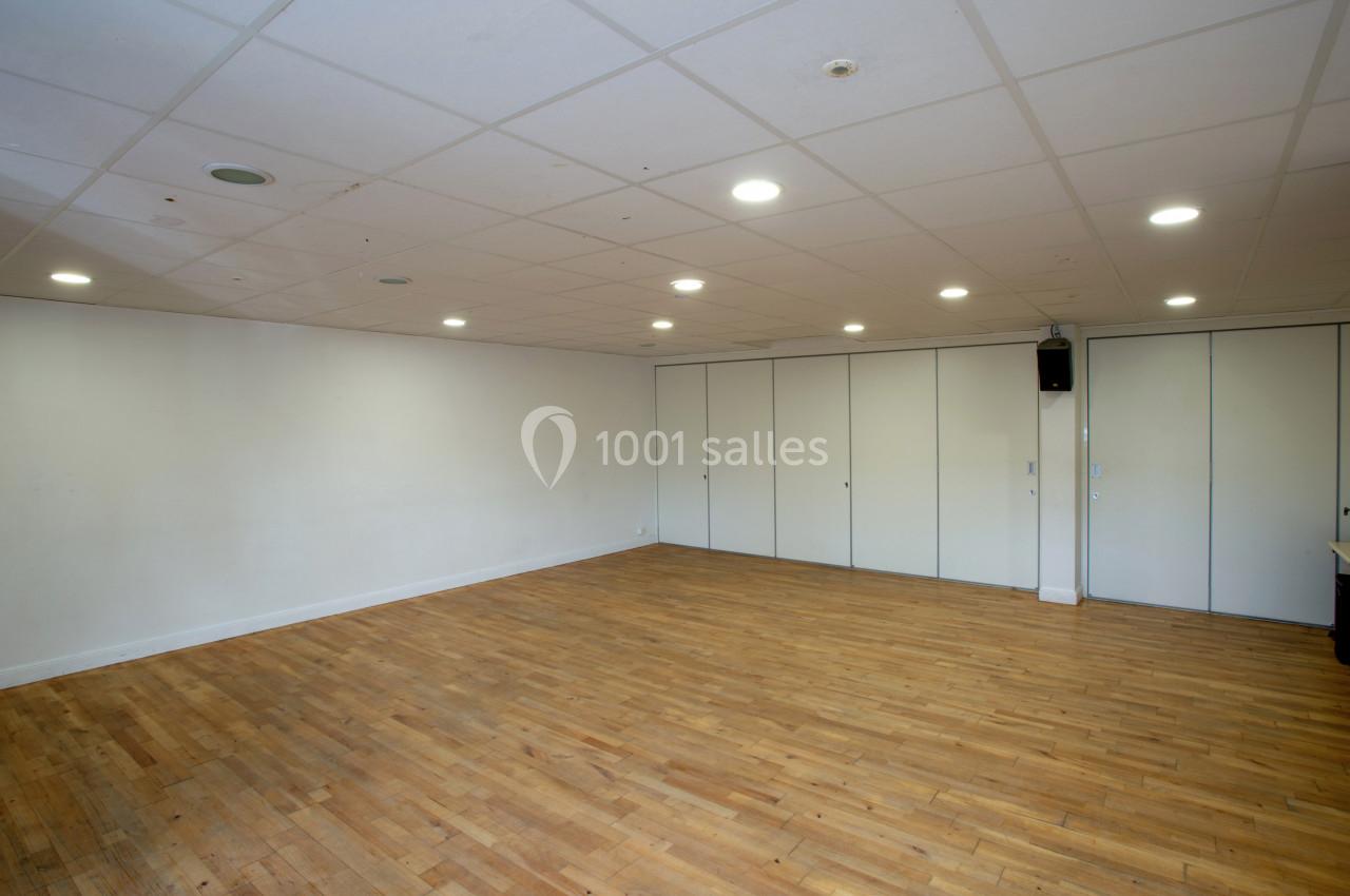Salle vide avec parquet en bois clair, murs blancs, plafond avec éclairage encastré et portes pliantes blanches.