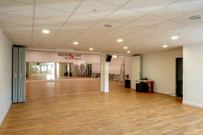 Vue d'un jardin clôturé avec pelouse, deux pots rouges contenant des plantes et un premier plan de feuilles vertes.