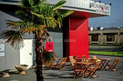 Vue d'un jardin clôturé avec pelouse, deux pots rouges contenant des plantes et un premier plan de feuilles vertes.