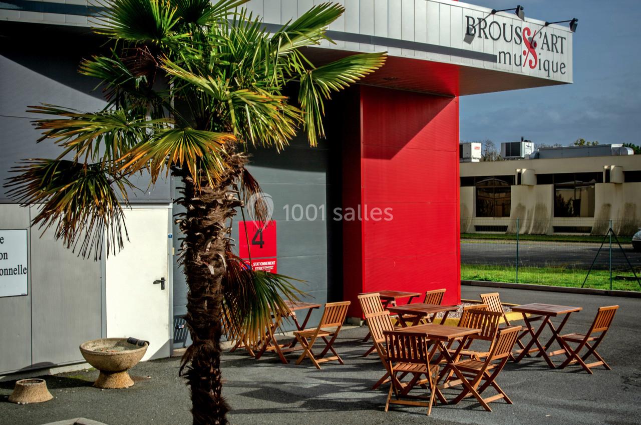 Façade d'un bâtiment avec une enseigne ’Brouss'Art Musique’, terrasse aménagée avec des tables et chaises en bois.