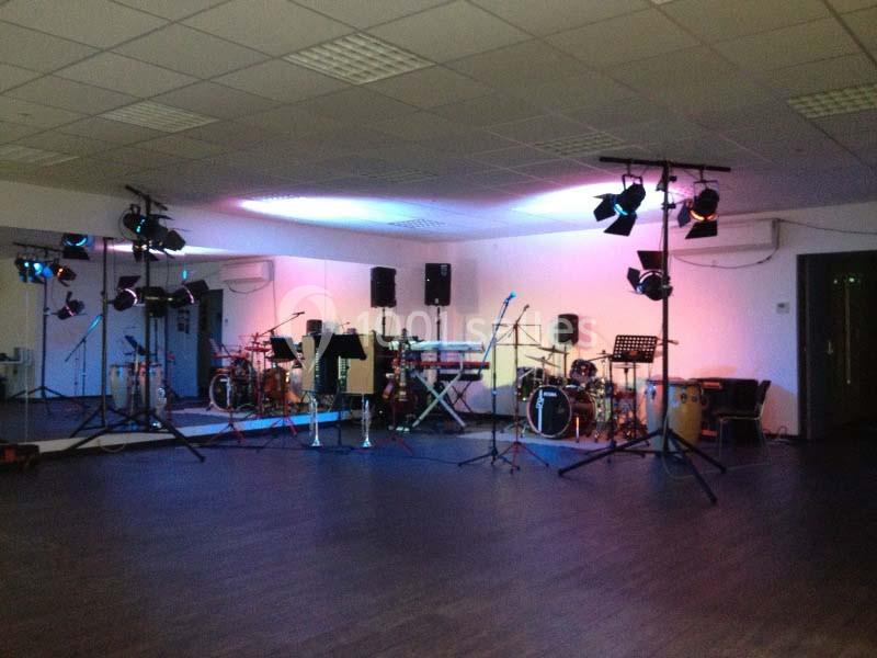 Salle de répétition équipée d'instruments de musique, micros, éclairages colorés et miroirs sur un mur.