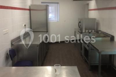 Vue d'un jardin clôturé avec pelouse, deux pots rouges contenant des plantes et un premier plan de feuilles vertes.