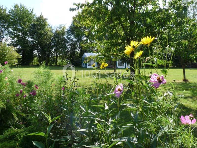 Jardin verdoyant avec des fleurs colorées au premier plan et une serre blanche en arrière-plan.