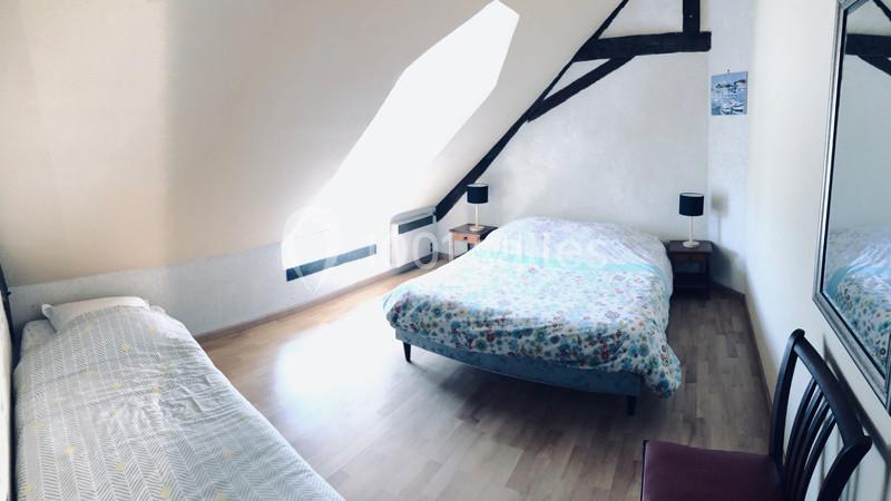 Chambre mansardée avec un lit double, un lit simple, des poutres apparentes, un miroir et un éclairage naturel.