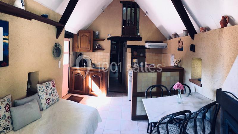 Vue d'une petite cuisine ouverte avec coin repas, canapé, poutres apparentes et décoration rustique.